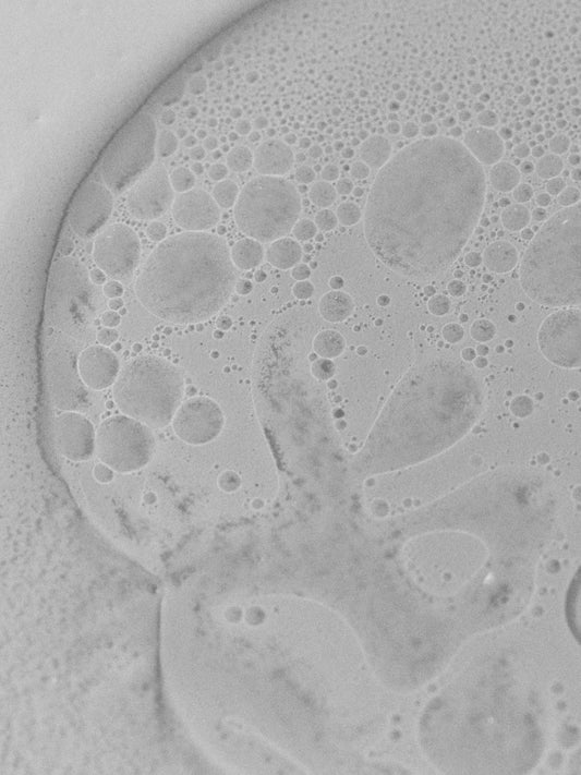 Black-and-white macro of an emulsion showing droplets suspended in a lighter matrix at microscopic scale.
