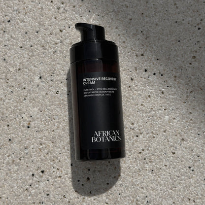 Black bottle of 'Intensive Recovery Cream' by African Botanics on a textured gray surface